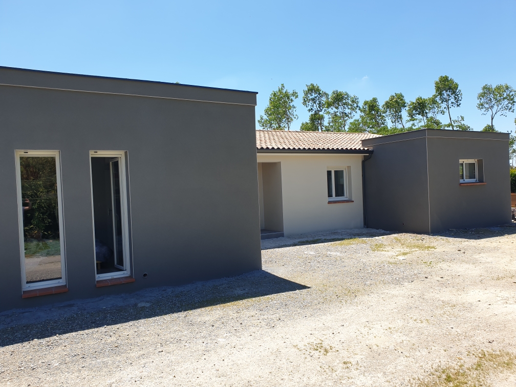 Extension moderne d’une maison avec façades grises et toit plat, reliant les volumes existants.