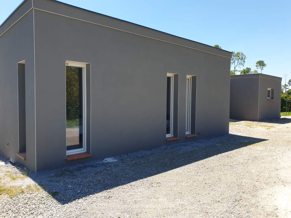 Volume d’extension à toit plat avec grandes ouvertures verticales sur façade grise.