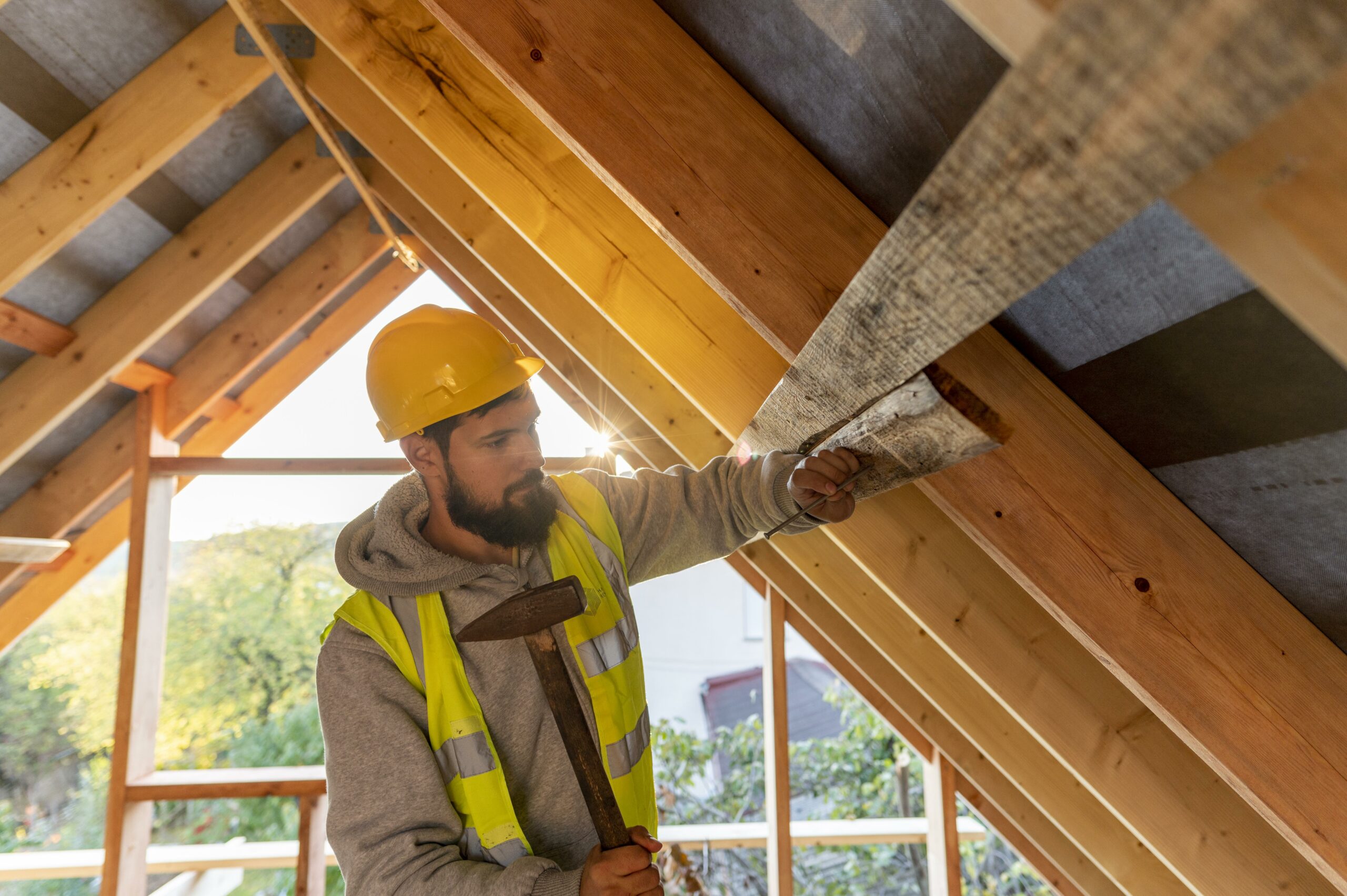 Artisan du bâtiment posant une planche de bois dans la charpente d’une maison en construction.